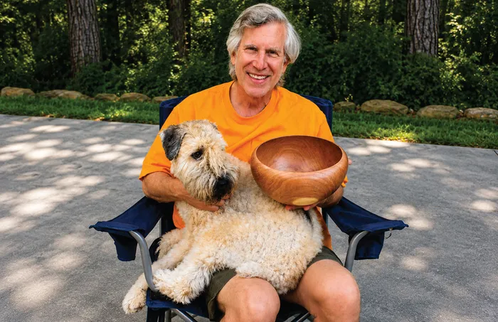 Russ in a camp chair holding a mesquite bowl, with Baxter the wheaten terrier on his lap